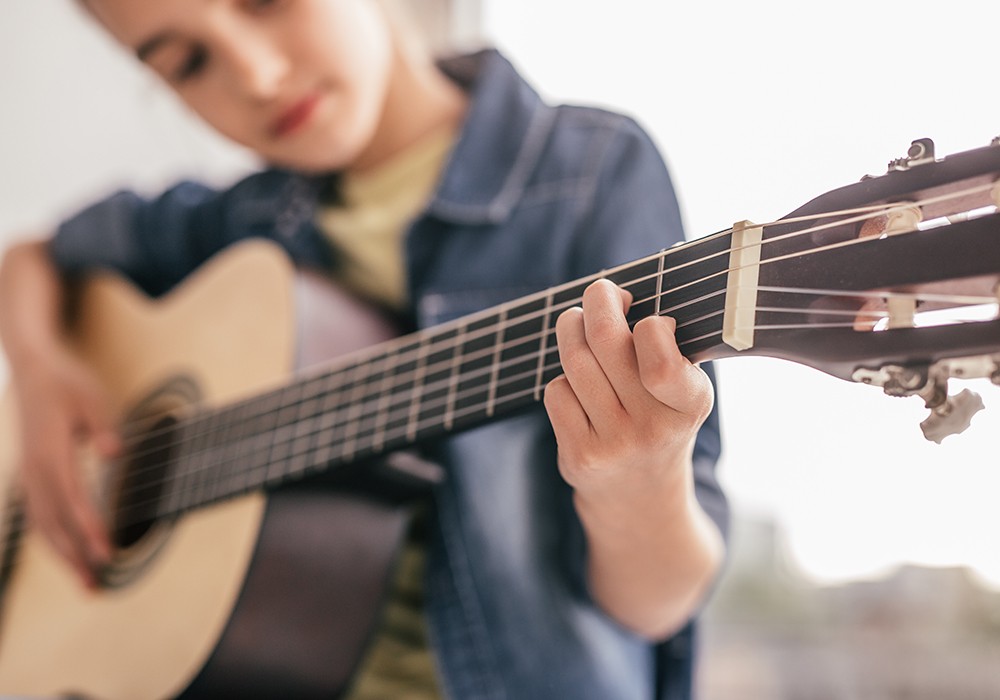 Mädchen lernt Akkorde auf der Akustikgitarre beim individuellen Musikunterricht zu Hause
