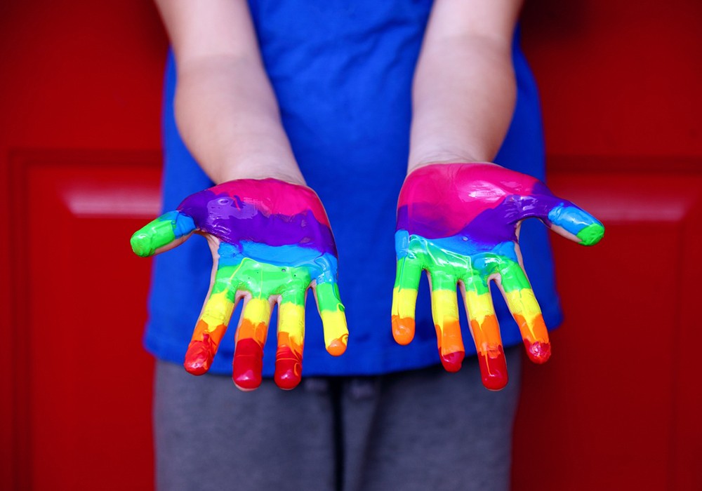 Kind zeigt Handflächen die mit Regenbogenfarben bemalt sind